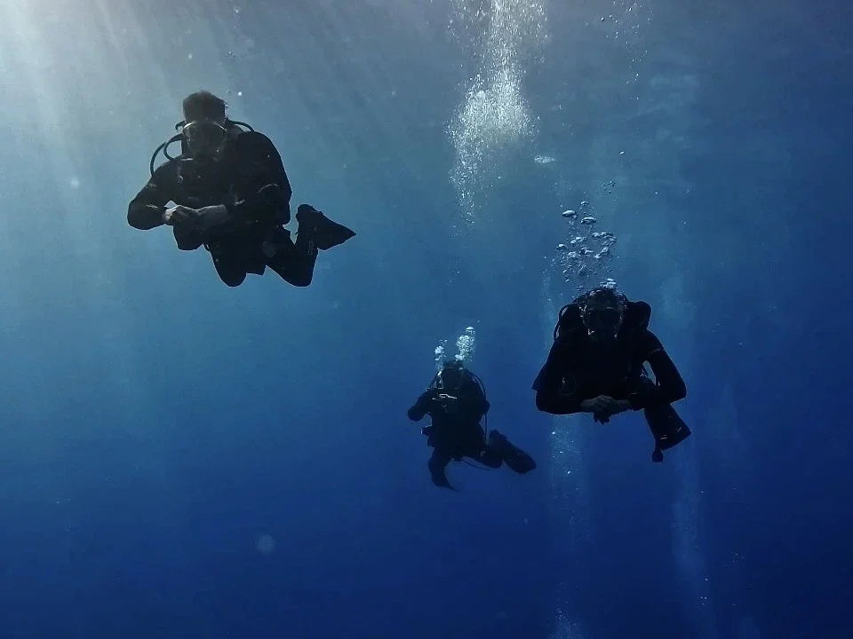 Three scuba divers descending into deep blue water during the SSI Deep adventure dive at Barbarian Diving Tenerife