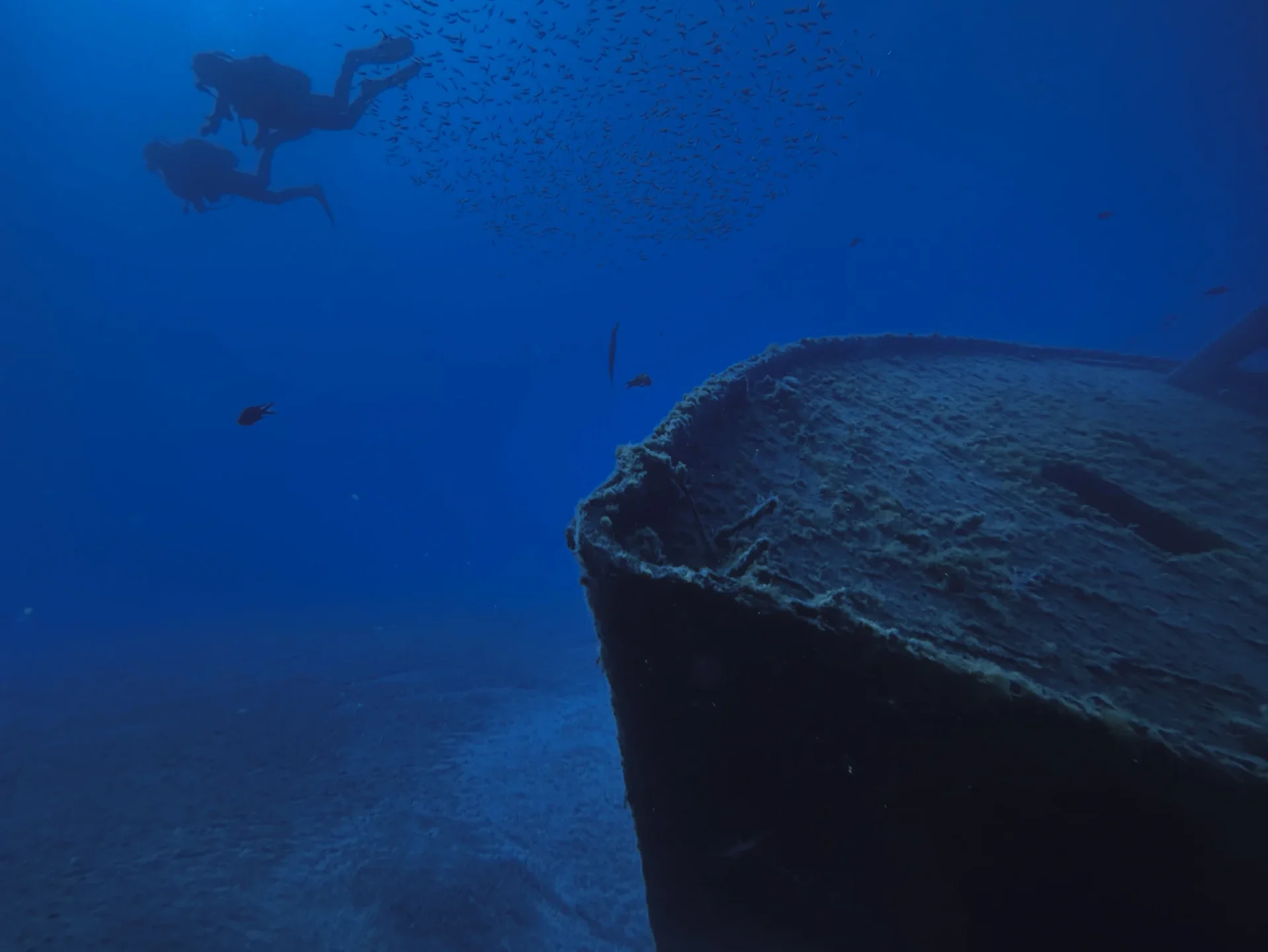 Two scuba divers silhouetted above the Twins wreck surrounded by a shoal of fish during the SSI Wreck adventure dive at Barbarian Diving Tenerife
